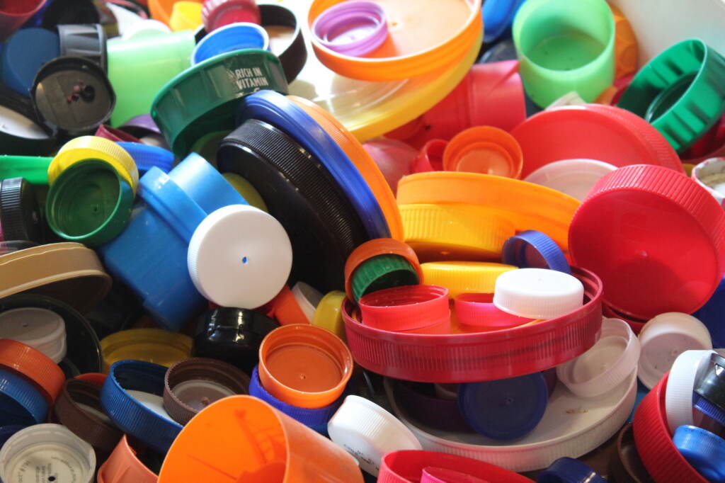 A close up of many different colors of plastic bottle caps thrown together.