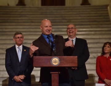 Mastriano speaks and gestures at a podium. Other men stand in the background.