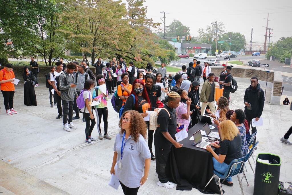 A group of students check in at a table outside of their high school.
