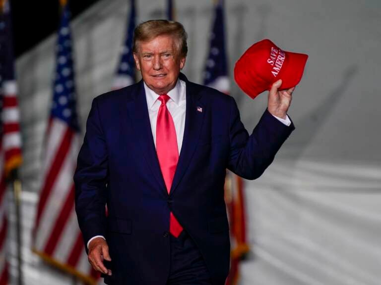 Former President Donald Trump holds up a red hat while on stage at a rally