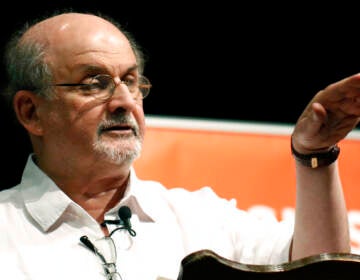 Salman Rushdie gestures as he speaks at a podium.