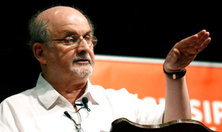 Salman Rushdie gestures as he speaks at a podium.