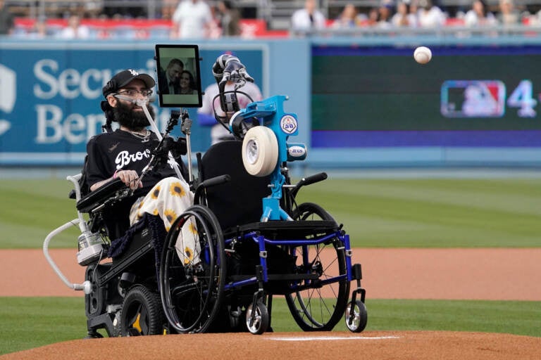 Anthony Carbajal, who is battling ALS (Lou Gehrig's disease) throws out the ceremonial first pitch with the help of a pitching machine prior to a baseball game between the Los Angeles Dodgers and the New York Mets Thursday, June 2, 2022, in Los Angeles. (AP Photo/Mark J. Terrill)