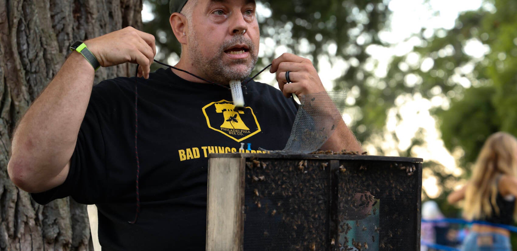 Don Shump prepares to have his ''bee beard'' made for a presentation at the 2022 Philadelphia Honey Festival. He’s tying the queen bee around his head, so the bee swarm will follow. (Kimberly Paynter/WHYY)