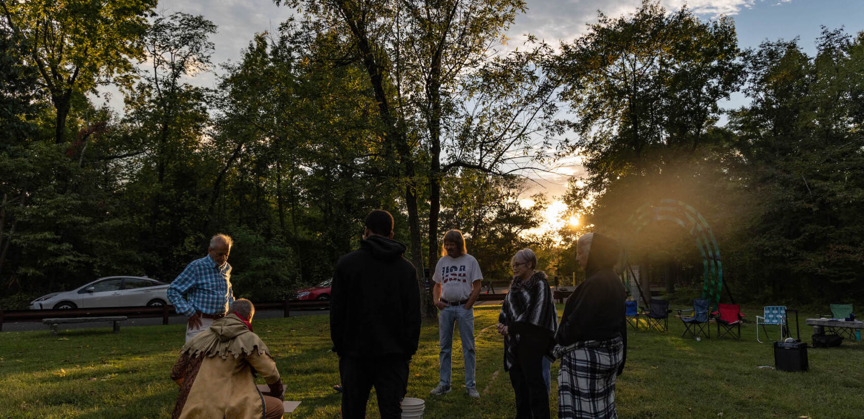 A group of people are gathered in a circle as the setting sun is visible behind them.