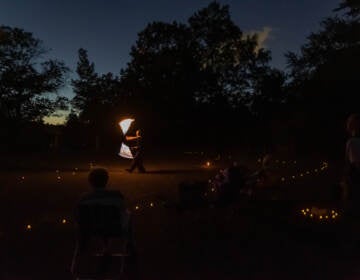 A person performs fire spinning in a darkened field as people look on.