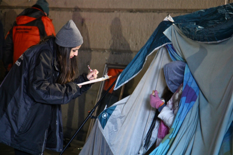 An outreach worker gets information from a woman living in a tent under the Emerald Street railroad overpass. (Emma Lee/WHYY)