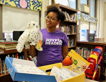 A woman in a purple shirt holds a stuffed owl in a classroom.