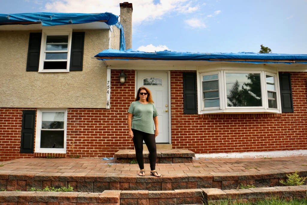 Tammy Echevaria stands in front of her home, which has blue tarp over the roof