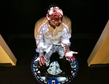 Joseph Lazaro Rodriguez crouches beneath his digital projection, ''Chromatherapeutics: Veritas DS,'' on display at the National Liberty Museum. Rodriquez's works complement the museum's exhibit about truth. (Emma Lee/WHYY)