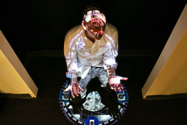 Joseph Lazaro Rodriguez crouches beneath his digital projection, ''Chromatherapeutics: Veritas DS,'' on display at the National Liberty Museum. Rodriquez's works complement the museum's exhibit about truth. (Emma Lee/WHYY)