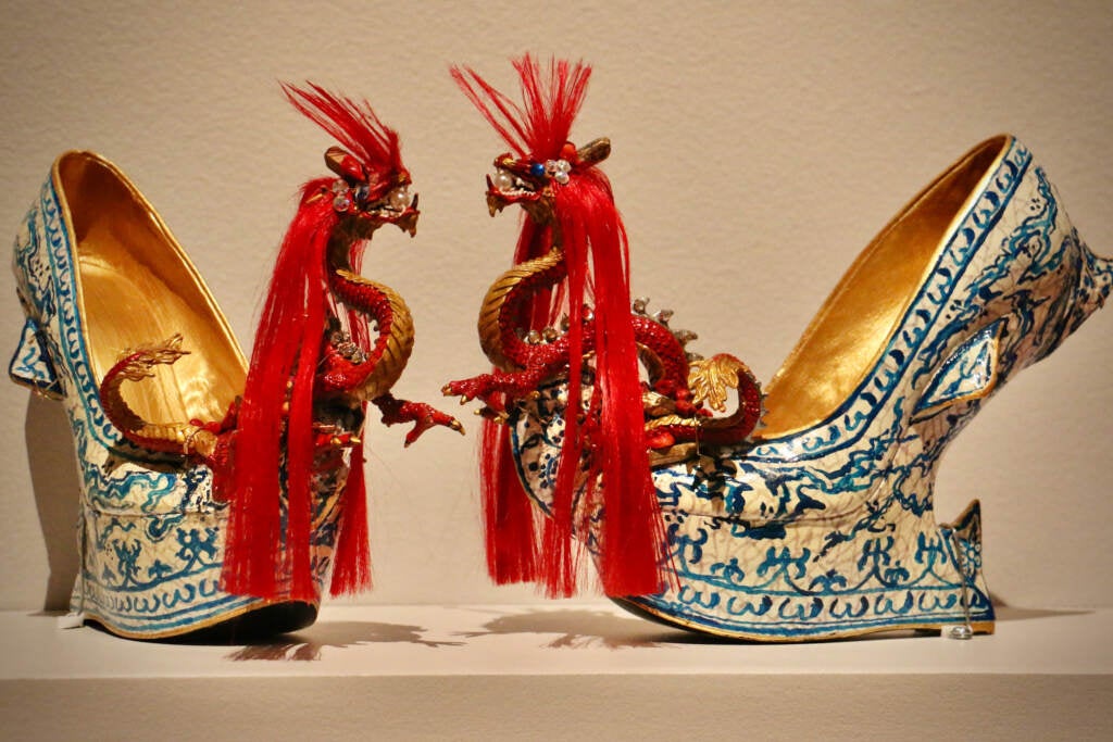 A pair of heel-less shoes are decorated with a dragon replica at the toe.
