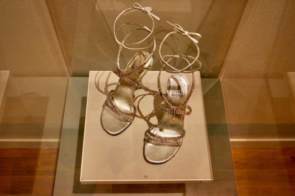 A pair of decorated sandals are in a glass case.