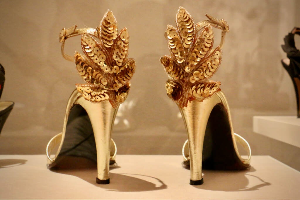 A close-up of a pair of gold high heels with sequined feathers at the back of the heel.