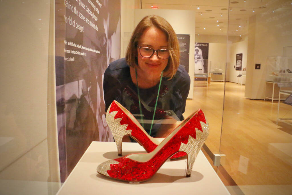 A woman looks at a pair of high-heeled shoes in a glass case.