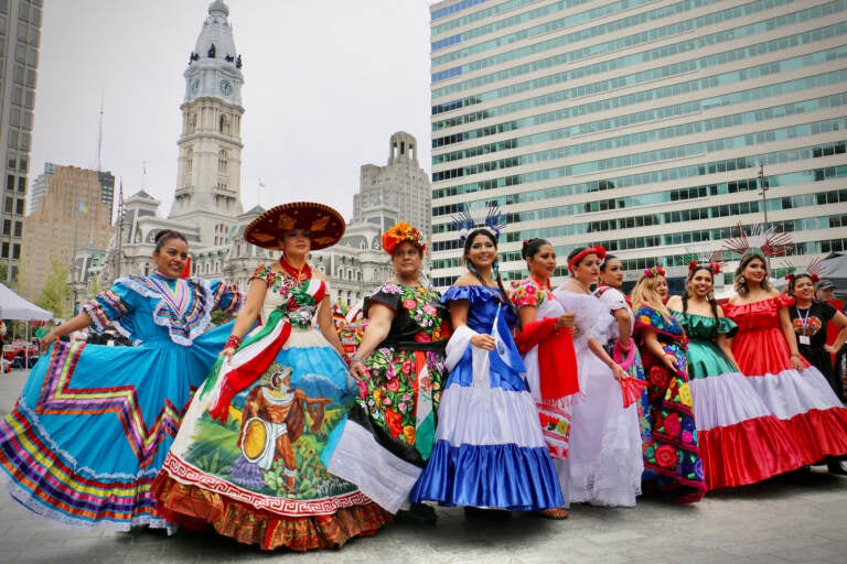 Women in dresses representing Latin American countries pose for photos at the Latin America Thrives in Philadelphia event in Love Park. (Emma Lee/WHYY)