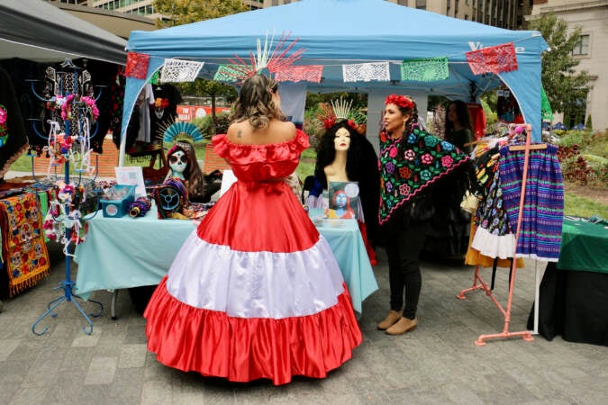 A woman in a red and white dress representing Peru stops at a stall selling Mexican clothing and crafts at the Latin America Thrives in Philadelphia event in Love Park. (Emma Lee/WHYY)