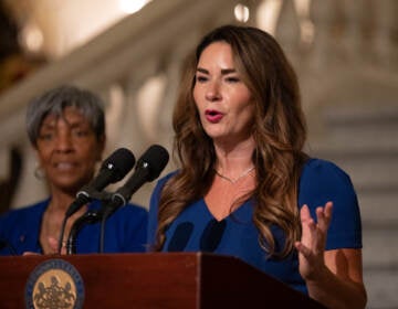 A woman gestures at a podium while she speaks into a microphone.