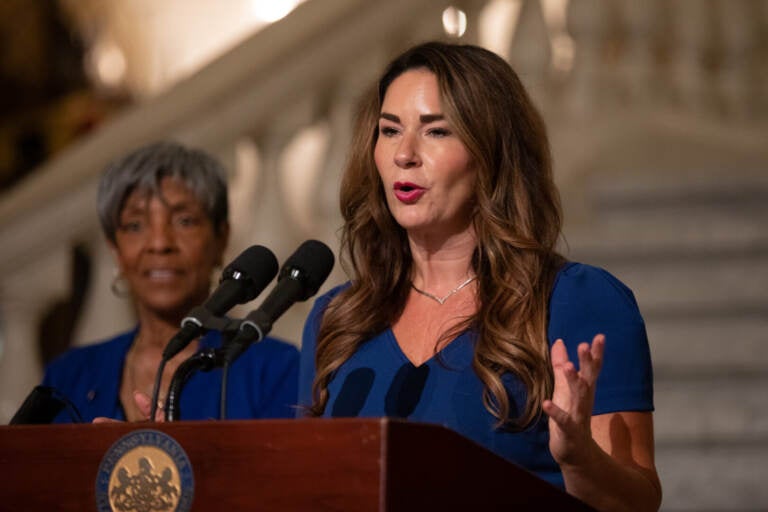 A woman gestures at a podium while she speaks into a microphone.