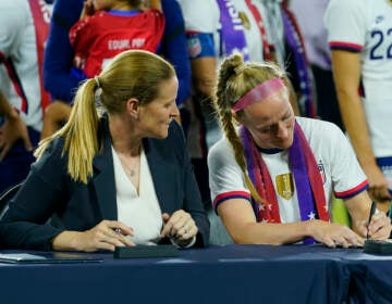 Cindy Parlow Cone, left, president of the U.S. Soccer Federation, looks on as United States' Becky Sauerbrunn signs a new collective bargaining agreement as part of an event in which with the federation, U.S. Women's National Team Players Association and the U.S. National Soccer Team Players Association signed new collective bargaining agreements following the women's match against Nigeria at Audi Field, Tuesday, Sept. 6, 2022, in Washington. The U.S. won 2-1. (AP Photo/Julio Cortez)