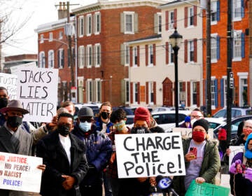 People gather holding signs that read Charge the police. Rowhomes are visible in the background.