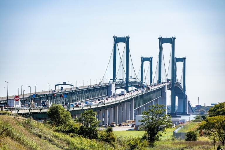 The Delaware Memorial Bridge is shown from afar, with a blue sky in the background.