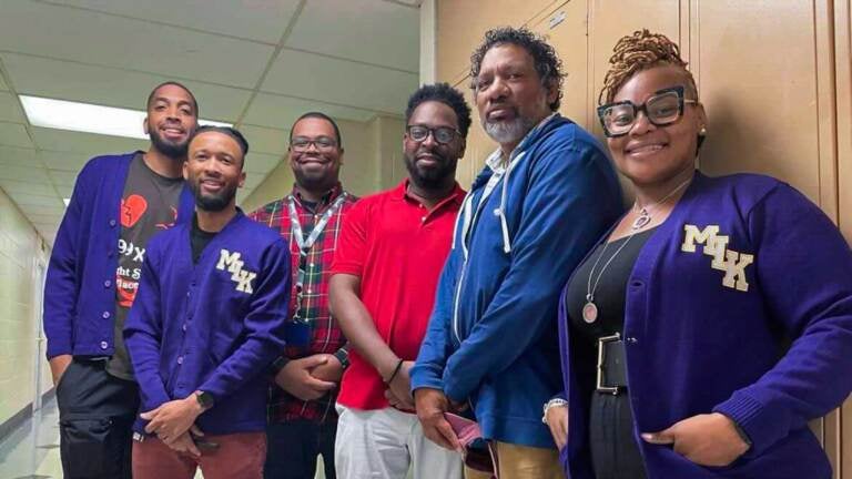 Teachers at Philadelphia’s Martin Luther King High School (from left) Marsalis Chism, Eric Butler, Michael Flemming, Stephen Flemming, and Denzil Flemming stand next to Principal Keisha Wilkins in the school’s hallway. (Johann Calhoun/Chalkbeat)