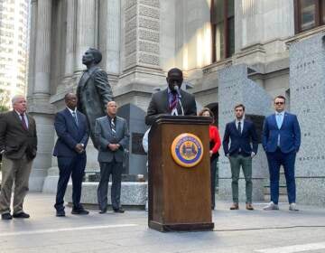 Councilmember Thomas speaks at a podium outside of City Hall surrounded by other people.