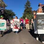 A group of people wearing signs representing banned books march down a street.