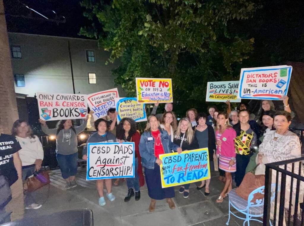 A group of people are gathered together at nighttime holding signs against censorship and banned books.