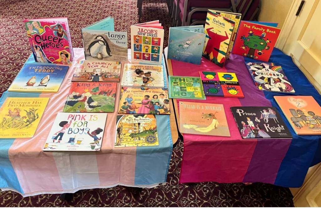 A table draped with the transgender rights and Pride flags has picture books displayed on it.