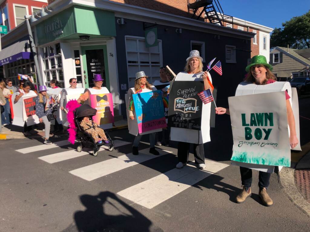 A group of people wearing signs representing banned books stand together in a crosswalk