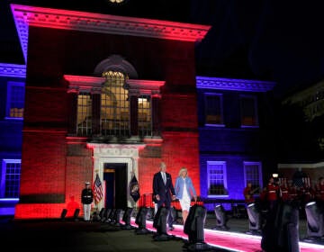 President Biden and First Lady Jill Biden walk out from Independence Hall lit with red and blue lights.