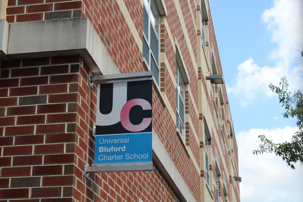 A sign reads: UC, Universal Bluford Charter School. It's hanging from the side of a red brick building.