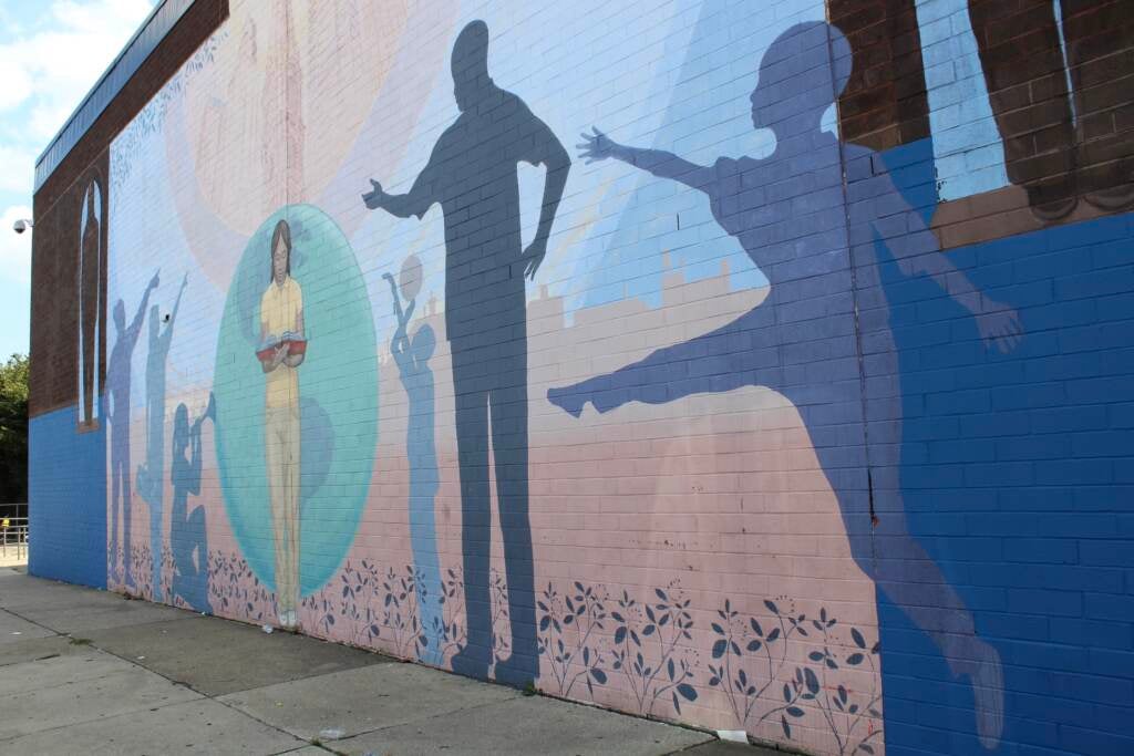 Silhouettes of children jumping, playing basketball, and reading are visible on a brick wall on the side of a building.