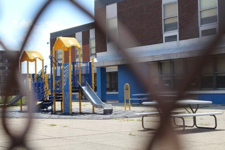 A playground is visible through the links of a fence.