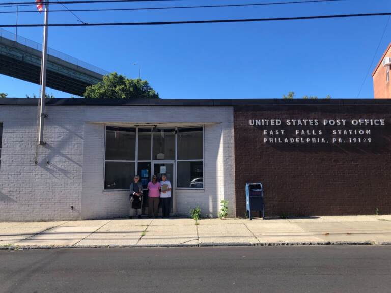 Three people stand in front of a building which reads 