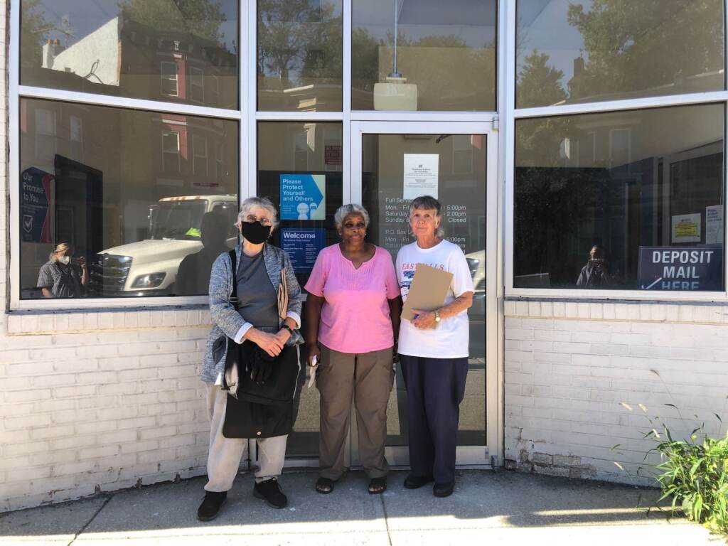 Three people stand in front of the glass windows of a building.