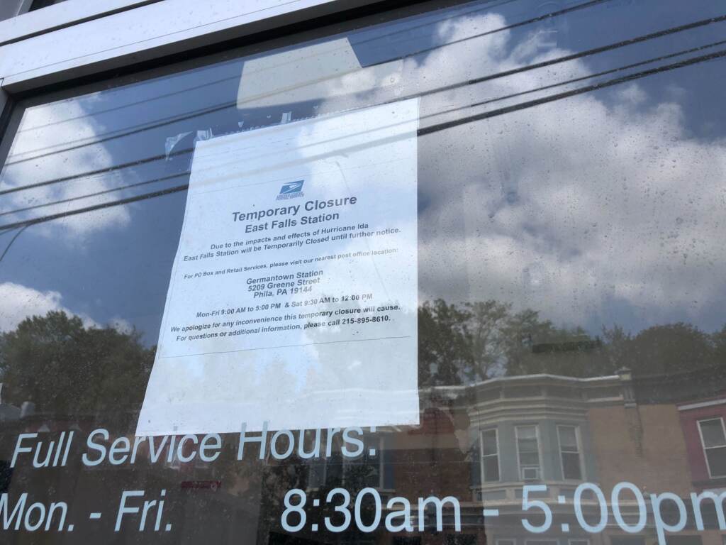 A sign reads "Temporary Closure East Falls Station" and is posted in a window. The reflection of rowhomes from across the street is visible in the windo.