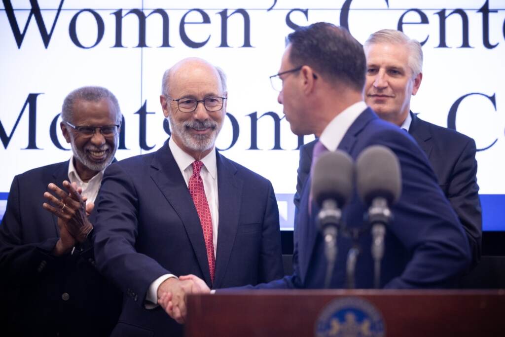 AG Josh Shapiro turns towards Gov. Tom Wolf and shakes his hand. Rep. Todd Stephens is visible in the background.