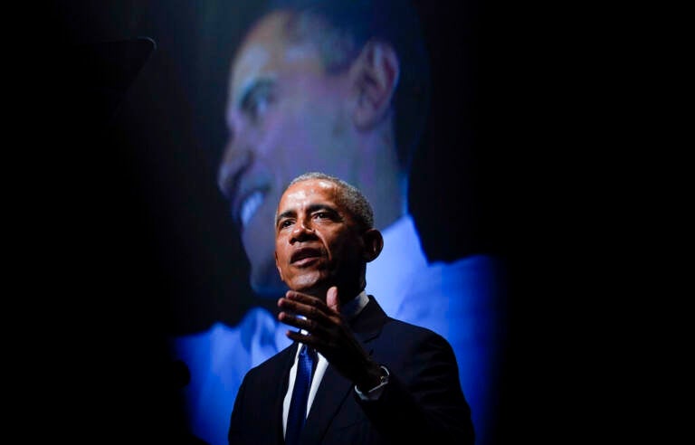 Obama speaks on stage, with an image of Obama showing in the background.