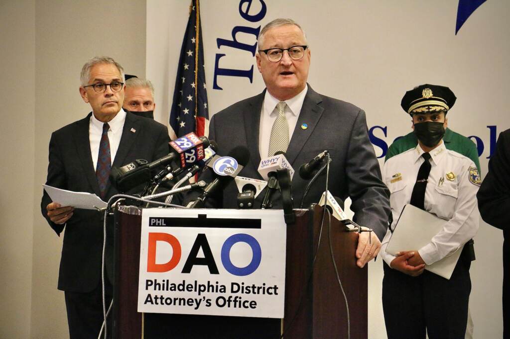 Mayor Jim Kenney stands at a podium with a number of microphones. DA Kasner is standing to the left, and Police Chief Danielle Outlaw to the right, as they both look on.