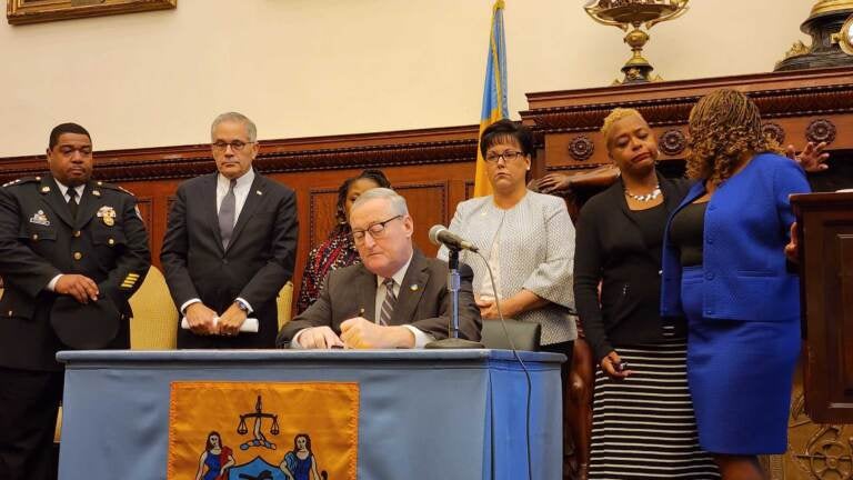 Mayor Kenney signs a document at a table surrounded by other elected officials.