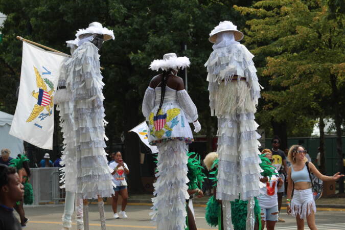 Three people walk on stilts, towering over other people walking around.