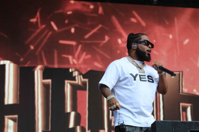 A performer sings into a microphone with a screen visible behind him.