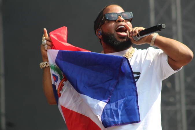 A performer sings into a microphone while holding the flag of the Dominican Republic.