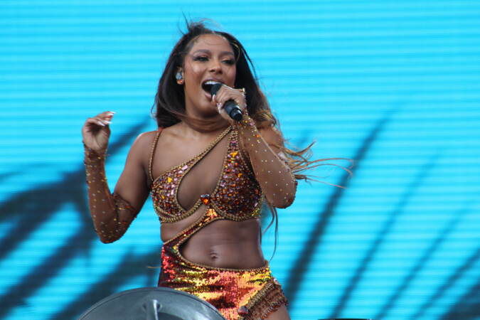 A singer sings into a microphone with a blue screen visible behind her.