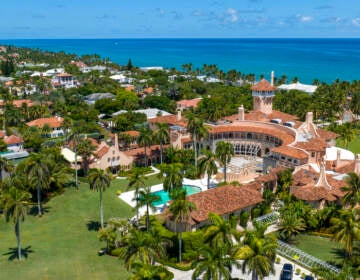 A view from above of a sprawling building with a pool and green laws, with a beach and ocean in the background.