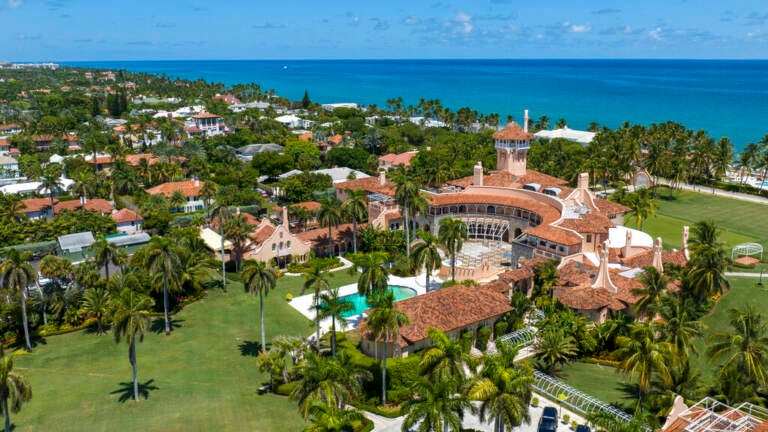 A view from above of a sprawling building with a pool and green laws, with a beach and ocean in the background.