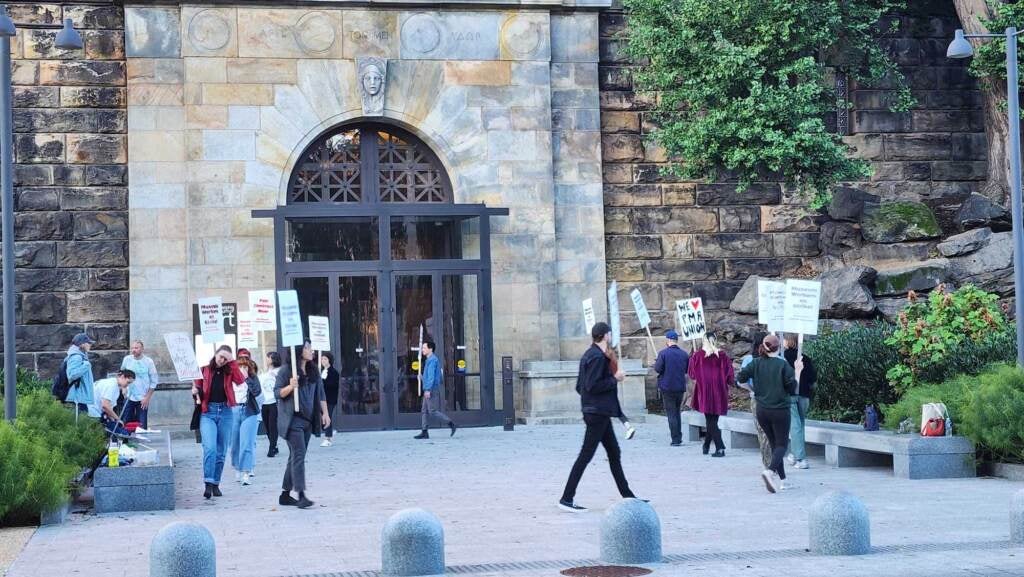People hold signs walking around in a circle in front of a stone building.